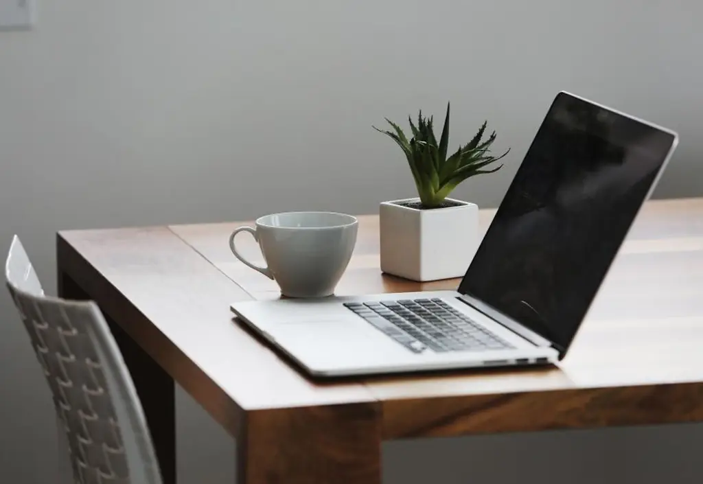 A laptop open on a video call, a breakfast bowl and a notebook on a kitchen table